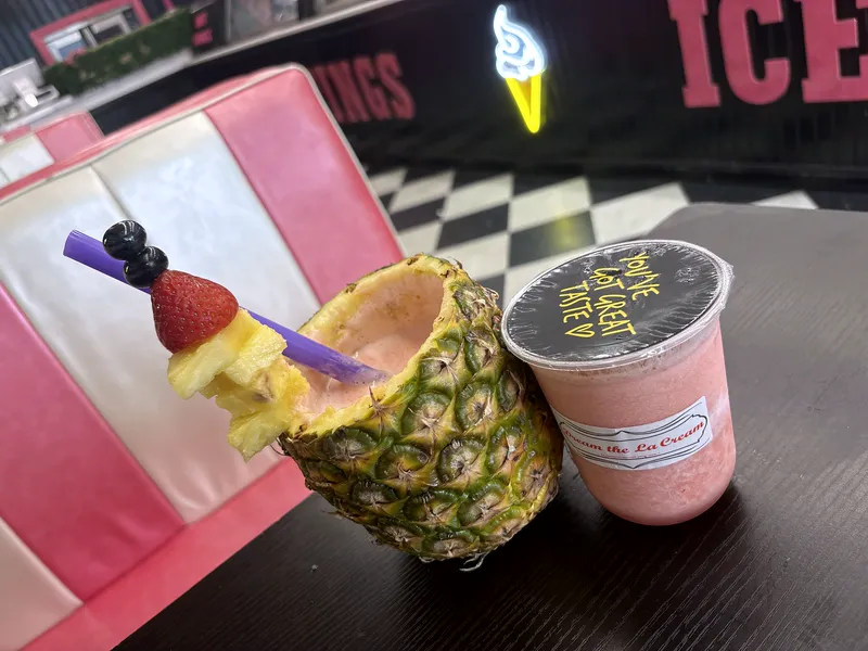 A Dream Pineapple cup with a fruit skewer, next to a strawberry drink with a Dream the La Cream lid