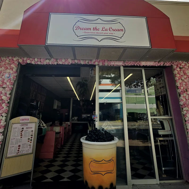 The storefront on Atlantic Avenue: a red arched awning, the Dream the La Cream sign, a wall of pink and white flowers and a giant bubble tea cup